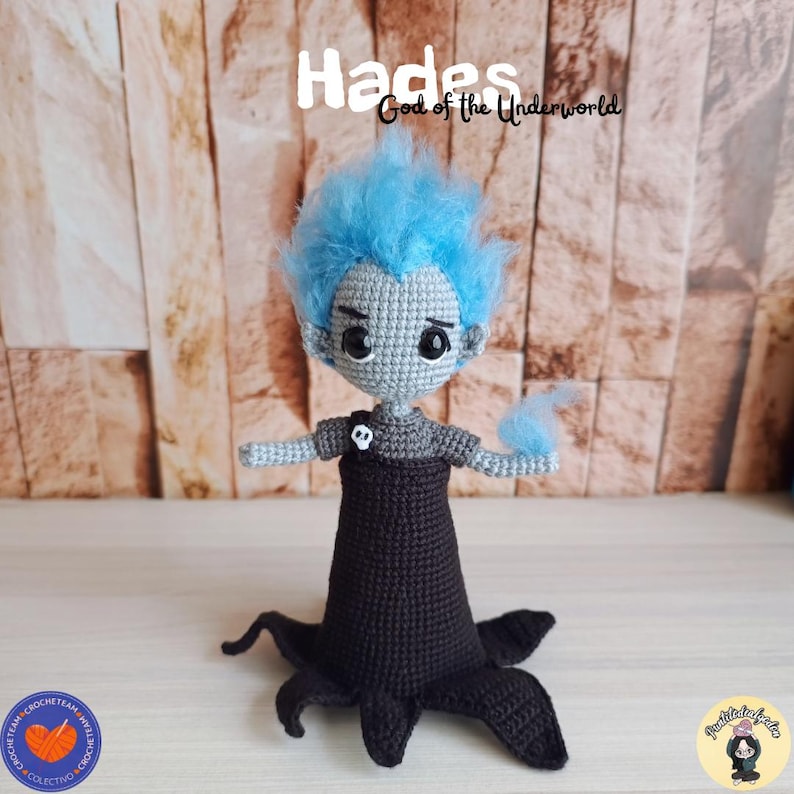 K&ouml;nnte beinhalten: Geh&auml;kelte Hades-Puppe mit blauen Haaren und einem schwarzen Outfit. Die Puppe hat ein graues Gesicht und Arme mit einem Totenkopfdetail auf der Brust. Der Text "Hades God of the Underworld" steht &uuml;ber der Puppe.