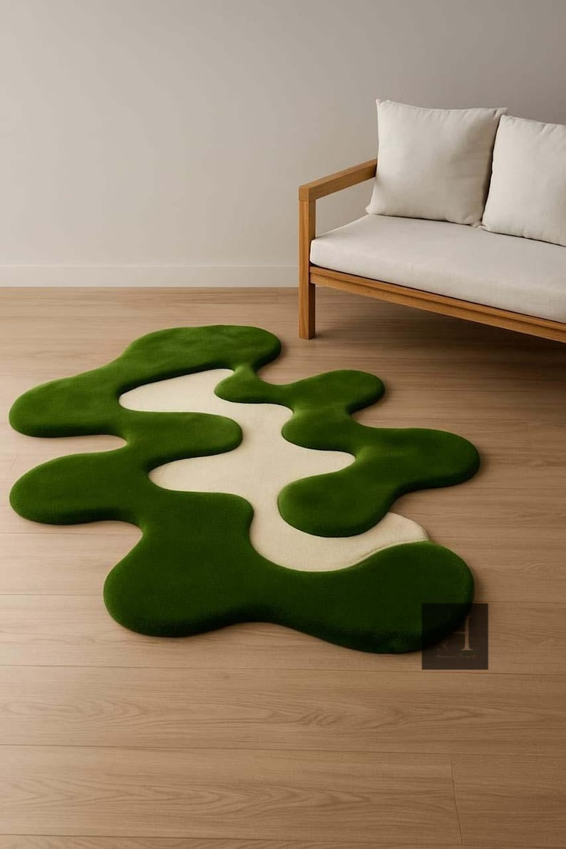 May include: A unique, abstract rug with a flowing, organic design. The rug features a vibrant green border that surrounds a cream-colored center. The rug is placed on a light-colored wooden floor, with a wooden sofa in the background.
