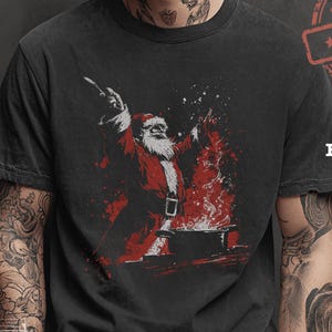 May include: Black graphic t-shirt featuring a red and white illustration of Santa Claus with a fiery background. The shirt has a distressed look and the text "MADE IN U.S.A." is visible. The word "Black" is also printed on the shirt.