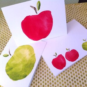 May include: Three white cards with hand-painted red and green apples. The cards are blank and ready for a message.