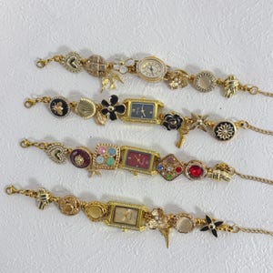 Könnte beinhalten: Vier goldfarbene Armbänder mit verschiedenen dekorativen Elementen. Jedes Armband hat ein Zifferblatt und eine Auswahl an Charms, darunter Herzen, Blumen und geometrische Formen. Die Armbänder werden auf einer weißen Oberfläche präsentiert.