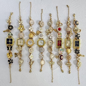 Pode incluir: Uma coleção de oito pulseiras de berloques douradas, cada uma com um pequeno mostrador de relógio. As pulseiras são adornadas com vários berloques, incluindo flores, corações e borboletas. Os mostradores dos relógios têm diferentes formas e cores, incluindo quadrados, redondos e retangulares.