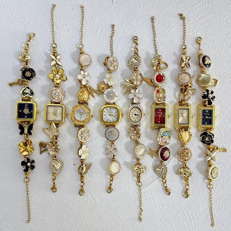 May include: A collection of eight gold-toned charm bracelets, each featuring a small watch face. The bracelets are adorned with various charms, including flowers, hearts, and butterflies. The watch faces have different shapes and colors, including square, round, and rectangular.