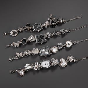 May include: Four silver charm bracelets with square watch faces. Each bracelet features decorative charms, including hearts, butterflies, flowers, and pearls. The watch faces have black or silver dials. The bracelets are set against a dark grey background.