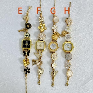May include: Four gold-toned bracelet watches with decorative charms. Each watch has a different face shape and is adorned with flowers, butterflies, and other embellishments. The watches are suspended from delicate chains.