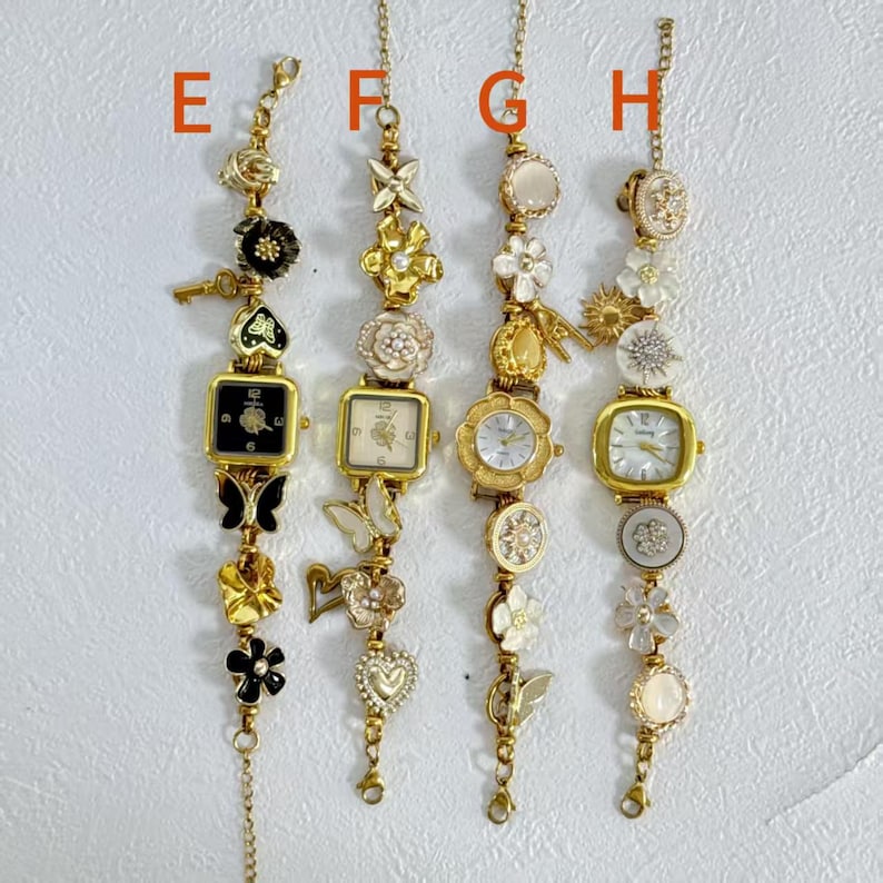 May include: Four gold-toned bracelet watches with decorative charms. Each watch has a different face shape and is adorned with flowers, butterflies, and other embellishments. The watches are suspended from delicate chains.