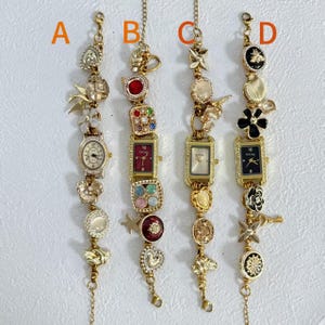 May include: Four gold-toned charm bracelets with decorative elements. Each bracelet features a watch face and various charms, including flowers, hearts, and geometric shapes. The watches have different colored faces and are adorned with rhinestones.