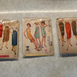 May include: Three vintage sewing pattern envelopes in clear plastic sleeves. The left envelope is Simplicity 1345, the center is McCall's 6740, and the right is McCall's 4680. Each envelope features illustrations of various skirt and dress designs.