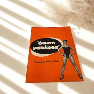 Peut inclure: Programme de comédie musicale vintage orange "Damn Yankees". La couverture présente une illustration en noir et blanc d'une femme en maillot de bain, avec le titre dans un ovale noir. Le texte "THE SMASH HIT MUSICAL COMEDY" est en dessous du titre.