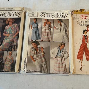 May include: Three vintage Simplicity sewing pattern envelopes featuring illustrations of various clothing styles including blazers, skirts, trousers, and vests. The paper envelopes display printed text, model photographs, and size information for garment construction.