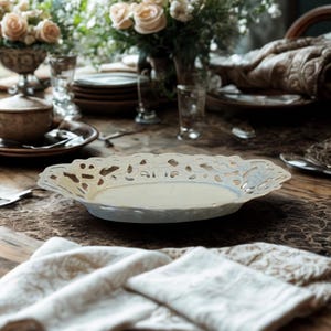 May include: An oval ceramic serving dish featuring a wide, intricate openwork filigree border with a smooth, cream-colored center. The dish has a glossy finish and a delicate, lace-like pattern along the edges, presenting a shallow, flat profile.
