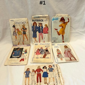 May include: A collection of vintage sewing patterns featuring illustrations of clothing designs. The patterns are from brands like Simplicity and Butterick, with images of dresses, jackets, and other garments. The patterns are arranged on a white surface.