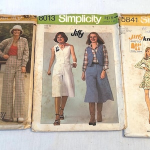 May include: Three vintage Simplicity sewing pattern envelopes labeled 5510, 8013, and 5841. The paper envelopes feature illustrations of various clothing styles including wide-leg trousers, a vest, a skirt, and a turtleneck sweater with pants.