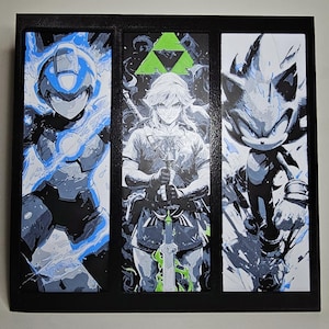 May include: A framed artwork featuring three panels with stylized illustrations of video game characters. The panels depict Mega Man in blue, Link from Zelda, and Sonic the Hedgehog, all in a graphic art style with a black frame.