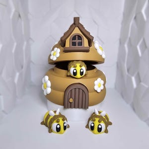 May include: A whimsical, brown, beehive-shaped figurine with a small door and a rooftop. The beehive is decorated with white daisy accents. Three cartoon bees with yellow and brown stripes are also present.