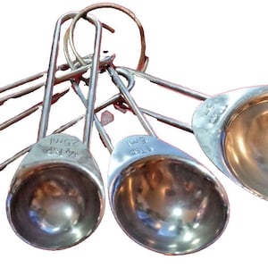 May include: A set of stainless steel measuring spoons, connected by a metal ring. The spoons vary in size, with measurements like 1/2 TSP and 5ml visible. The spoons have a shiny, reflective surface.