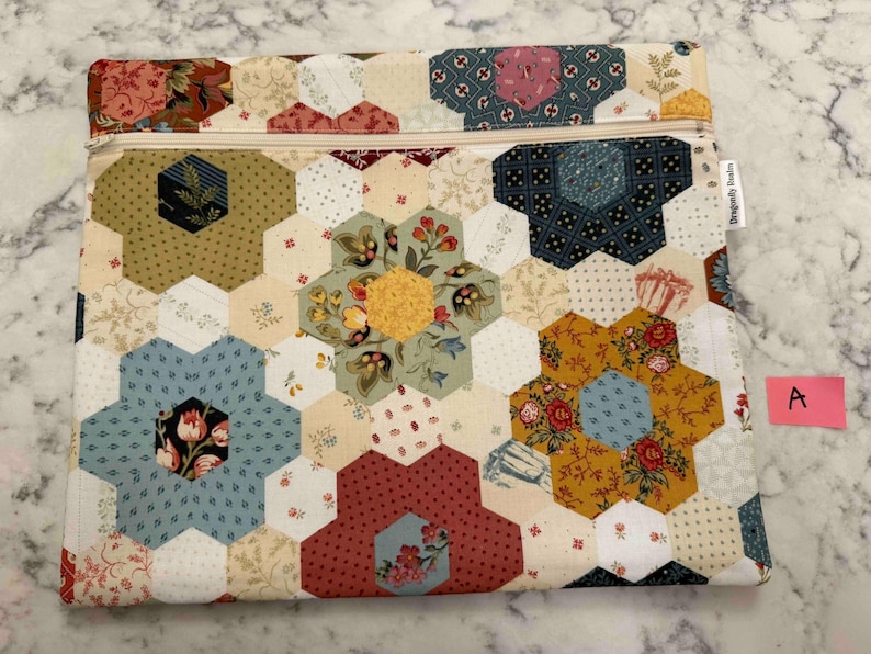 May include: A quilted fabric pouch with a zip closure. The pouch features a patchwork design of hexagonal shapes in various floral patterns and colours, including blue, red, yellow, and green. The zip is beige.