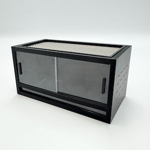 May include: A black terrarium with sliding glass doors and a mesh top. The rectangular enclosure has a dark frame and ventilation slits on the side. The glass doors are tinted, and the top is a fine mesh.
