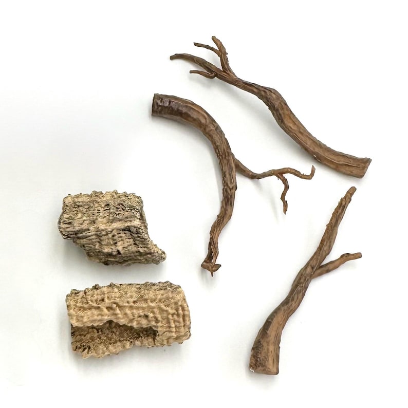 May include: A collection of decorative items resembling natural elements. The image shows several brown, twig-like branches and two pieces of textured, bark-like material, arranged against a white backdrop, highlighting their organic forms and hues.