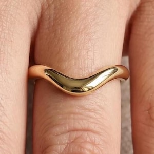 Peut inclure: Une bague dorée au design lisse et incurvé. La bague a une finition polie, reflétant la lumière. C'est un bijou simple et élégant.