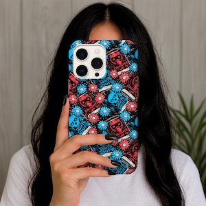 May include: A phone case with a black background featuring a repeating pattern of red and blue floral designs, skulls, and the text "LIGHTS OUT" and "CAUGHT UP". The case is held in front of a person.
