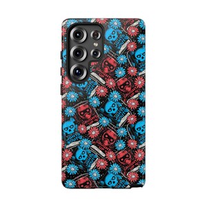 May include: A phone case featuring a repeating pattern of blue and red skulls, books, and flowers on a black backdrop. The books display the text "LIGHTS OUT" and "CAUGHT UP". The case has a camera module.