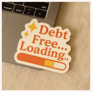 May include: A sticker with the words "Debt Free... Loading" in orange and white, with a loading bar graphic. The sticker is on a laptop keyboard.