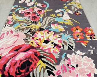 May include: A rectangular grey rug with a large floral pattern. The rug features flowers in pink, red, yellow, and blue. The flowers are arranged on a grey background. The rug has a soft, plush texture, suitable for a living room or bedroom.