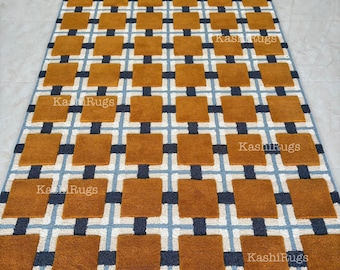 May include: A rectangular rug with a geometric pattern. The design features squares in shades of brown, navy blue, and light blue, arranged in a grid-like formation. The text "Kashi Rugs" is visible in several places on the rug.