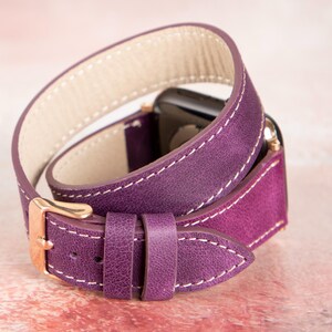 Puede incluir: Correa de cuero morado para Apple Watch con dise&ntilde;o de doble vuelta. La correa presenta costuras blancas y una hebilla dorada. La correa est&aacute; dise&ntilde;ada para envolverse dos veces alrededor de la mu&ntilde;eca.