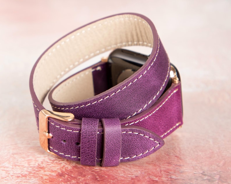Puede incluir: Correa de cuero morado para Apple Watch con dise&ntilde;o de doble vuelta. La correa presenta costuras blancas y una hebilla dorada. La correa est&aacute; dise&ntilde;ada para envolverse dos veces alrededor de la mu&ntilde;eca.