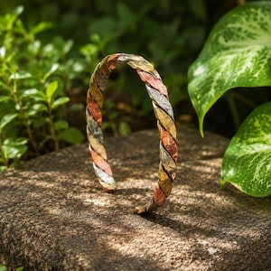 May include: A tri-color metal cuff bracelet featuring a twisted, braided design. The bracelet is constructed from alternating segments of copper, brass, and silver-toned metal, each with a textured, hammered finish throughout the entire band.