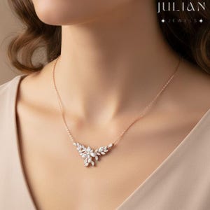 May include: Rose gold necklace with a floral design, featuring multiple clear gemstones. The necklace is centered with a cluster of stones and extends with leaf-shaped accents. The brand name "JULIAN JEWELS" is visible in the upper right corner.