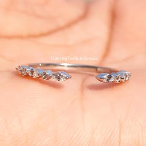 Op de afbeelding: Open zilveren ring met een rij kleine, heldere edelstenen. De ring is geplaatst tegen een vage achtergrond. De ring is een delicaat sieraad.