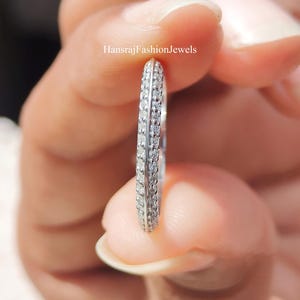 Op de afbeelding: Een zilveren ring met twee rijen kleine, heldere edelstenen. De ring wordt tussen de vingers gehouden, wat het delicate ontwerp benadrukt. De tekst "HansrajFashionJewels" is zichtbaar.