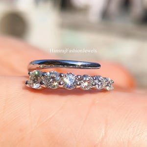 Könnte beinhalten: Ein silberfarbener Ohrklemme mit einer Reihe funkelnder, klarer Edelsteine. Die Klemme umschließt das Ohr, wobei die Edelsteine entlang der unteren Kurve angeordnet sind. Der Markenname "HansrajFashionJewels" ist sichtbar.