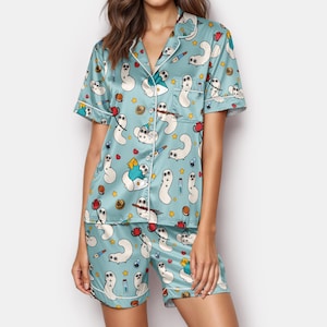 May include: Light blue pajama set with a whimsical pattern of white cartoon characters, stars, and other colorful illustrations. The set includes a short-sleeved button-up shirt and matching shorts, both trimmed with white piping.