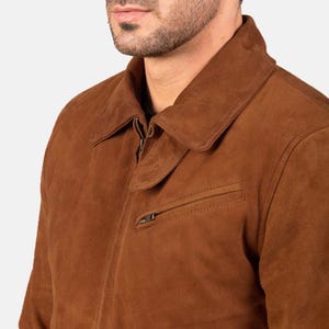 May include: A brown suede jacket with a collared neckline and a zipper closure. The jacket features a chest pocket with a zipper and a classic, tailored design. The color is a warm, earthy tone.