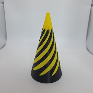 May include: A black and yellow cone-shaped object with a pointed top. The cone has alternating black and yellow stripes that spiral around the body. The top of the cone is solid yellow.