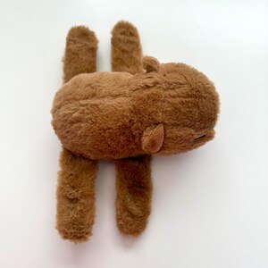 Puede incluir: Un peluche marr&oacute;n con forma de hipop&oacute;tamo. El juguete tiene una textura suave y peluda, con cuatro patas cortas y orejas peque&ntilde;as. El hipop&oacute;tamo est&aacute; tumbado boca abajo, con las patas extendidas.
