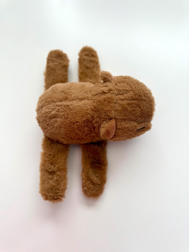 Puede incluir: Un peluche marr&oacute;n con forma de hipop&oacute;tamo. El juguete tiene una textura suave y peluda, con cuatro patas cortas y orejas peque&ntilde;as. El hipop&oacute;tamo est&aacute; tumbado boca abajo, con las patas extendidas.