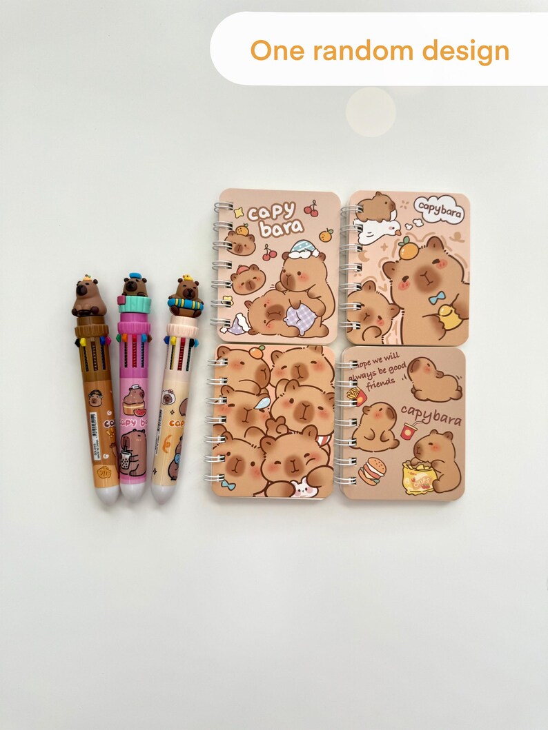 Puede incluir: Una colecci&oacute;n de art&iacute;culos de papeler&iacute;a con tem&aacute;tica de carpincho. La imagen incluye cuatro cuadernos peque&ntilde;os con espiral con ilustraciones y texto de carpinchos, junto con tres bol&iacute;grafos multicolores. Los cuadernos tienen una cubierta marr&oacute;n claro.