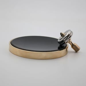 May include: A black and gold soap dish with a spinning top. The soap dish is round with a black center and a gold rim. The spinning top has a silver top and a gold stem.
