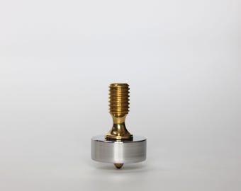 May include: A metal spinning top with a gold-colored threaded top and a silver-colored base. The top has a pointed tip for spinning. The background is plain white.
