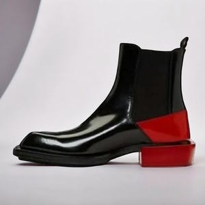May include: A black leather ankle boot with a red block heel. The boot features a sleek, glossy finish and a square toe design. The heel is approximately 2 inches high.