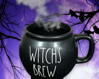 May include: A black cauldron-shaped mug with the words "WITCH'S BREW" in white lettering. Steam rises from the mug, suggesting a hot beverage. The background features a purple moon, bats, and bare tree branches, creating a Halloween theme.
