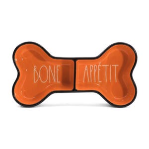 May include: Orange ceramic dog bowl in a bone shape with black trim. The words "BONE APPÉTIT" are written in white across the bowl. The bowl is divided into two sections.