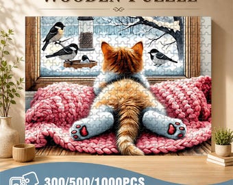 May include: Wooden jigsaw puzzle featuring a ginger and white cat looking out a window at birds in a snowy scene. The cat is lying on a pink blanket. The puzzle is available in 300, 500, and 1000 pieces.