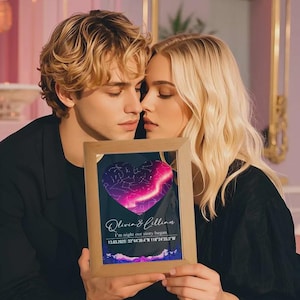 May include: A wooden framed print with a heart-shaped star map design. The print includes the names "Olivia & Lillian", the phrase "I'm night our story began", and coordinates. The frame is made of light-colored wood.