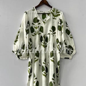 Puede incluir: Vestido blanco con estampado floral verde. El vestido tiene cuello en V, mangas largas y una silueta suelta y fluida. El diseño floral se repite en todo el vestido, creando un look cohesivo y elegante.